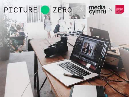 Photo of a wooden table with a camera and three laptops on it. On the top are logos for Picture Zero, Media Cymru and University of South Wales.