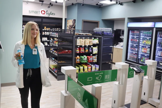 A health care worker at St. Joseph’s/Candler Hospital in Savannah, Georgia using AWS Just Walk Out Technology to grab food at a mini convenience store located in the medical facility. Health care worker is holding a blue beverage and snack. 
