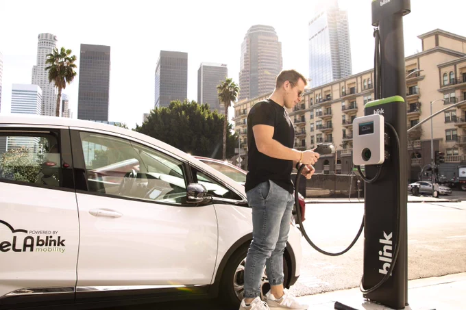 Man at a Blink Mobility station charging a Blue LA electric car
