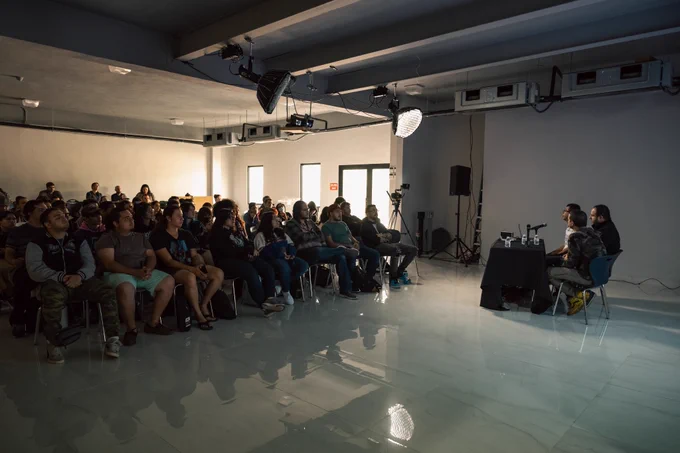 Fotografía de público sentados pendiente a el ex alumno Jonathan Martínez, el profesor José Ramos y el profesor Miguel Santiago, los cuales están hablando.