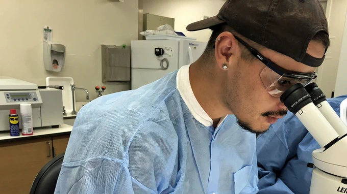 PHEFA participant Jacoby Clark wears a backward baseball cap and gazes into a white dual-eyed microscope.