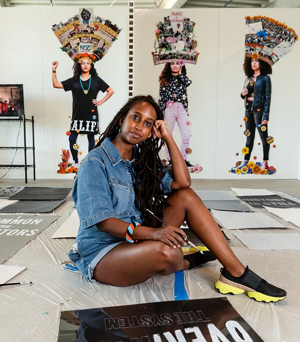 Artist Helina Metaferia sitting on the floor of her studio, looking at the camera with her head resting in her left hand.