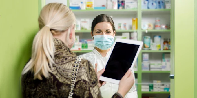 Pharmacist wearing facemask talks with adult patient