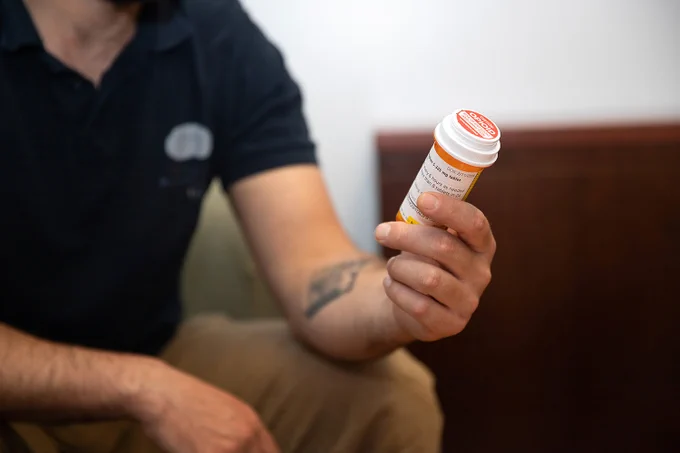 Photo of a man holding a prescription bottle with a red warning label reading "opioid"