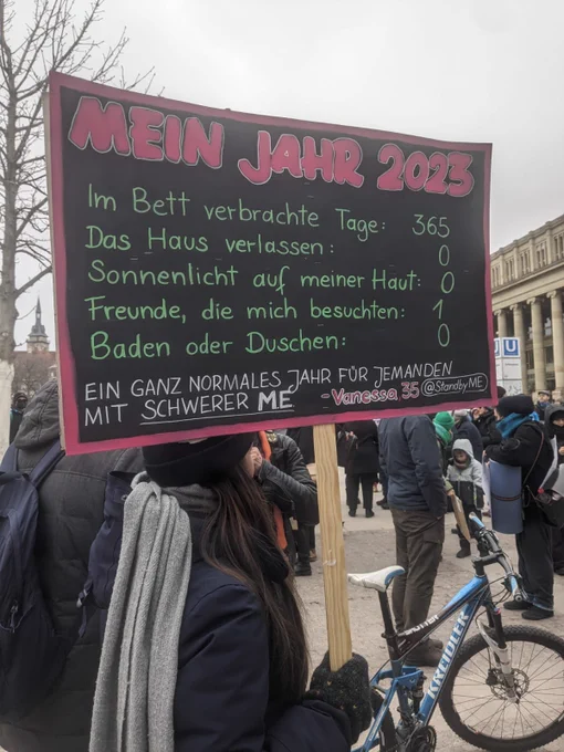 Demonstrandin hält schwarzes SChild mit folgender Aufschrift: Mein Jahr 2023. Im Bett verbrachte Tage: 365. Das Haus verlassen: 0. Sonnenlicht auf meiner Haut: 0. Freunde, die mich besuchten: 0. Baden oder Duschen: 0. Ein ganz normales Jahr für jemanden mit schwerer ME. Vanessa 35 @Standby_M_E