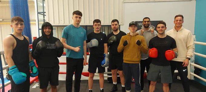 A group of young men standing together in a boxing ring. Some are wearing boxing gloves