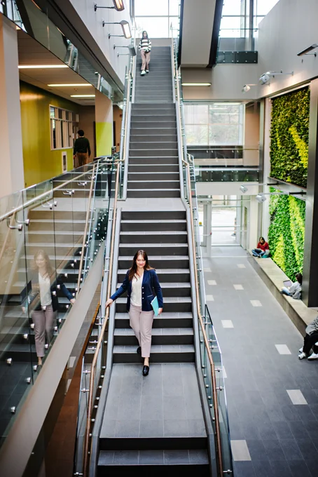 Natalie Majda walking down a long set of stairs in the University of Waterloo's environment building, surrounded by greenery.