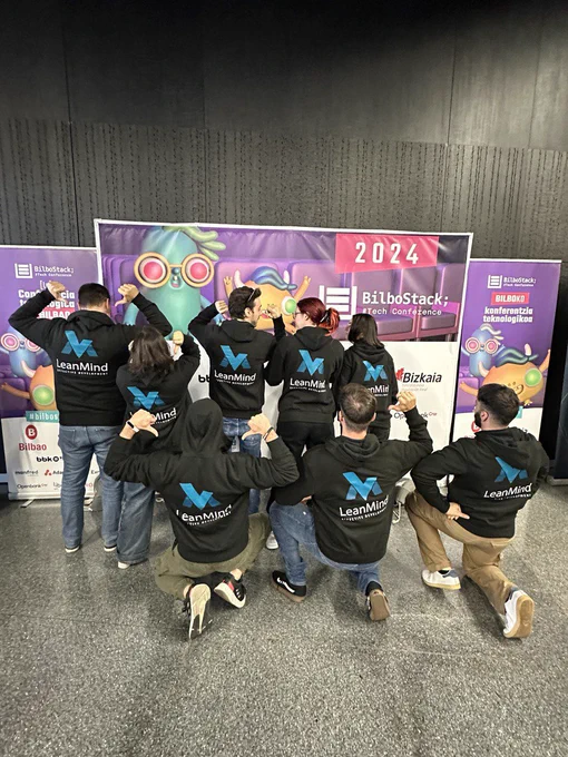 El mismo equipo de espaldas señalando con sus pulgares el logo de Lean Mind, se ve la M azul con la frase Efficient Development