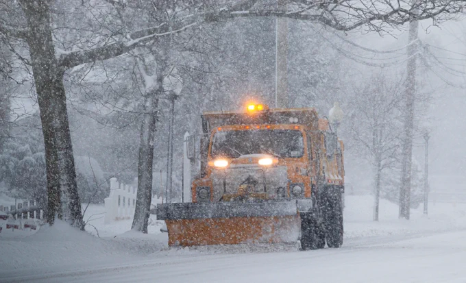 snow plow plowing a snow covered road as it continues to snow