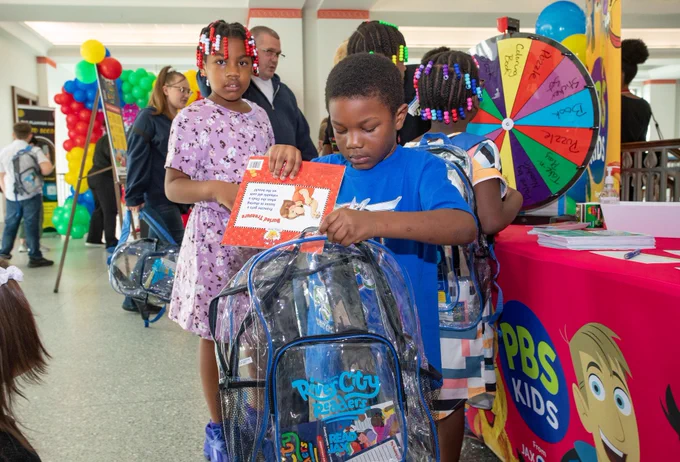 A boy in a blue shirt putting a book into a backpack