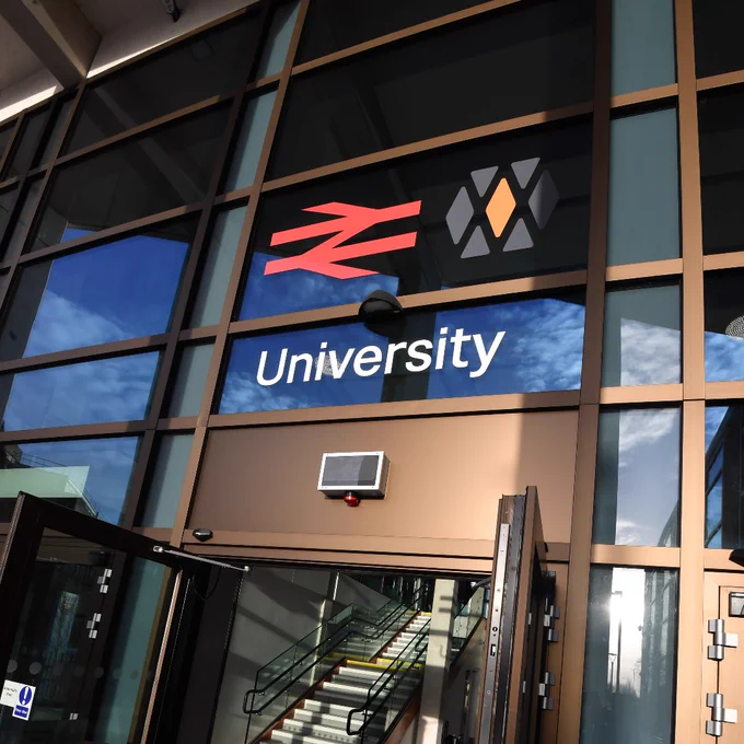 An image of the new University station front doors, with multiple glass panels, automatic door features and station façade signage and railway logos.