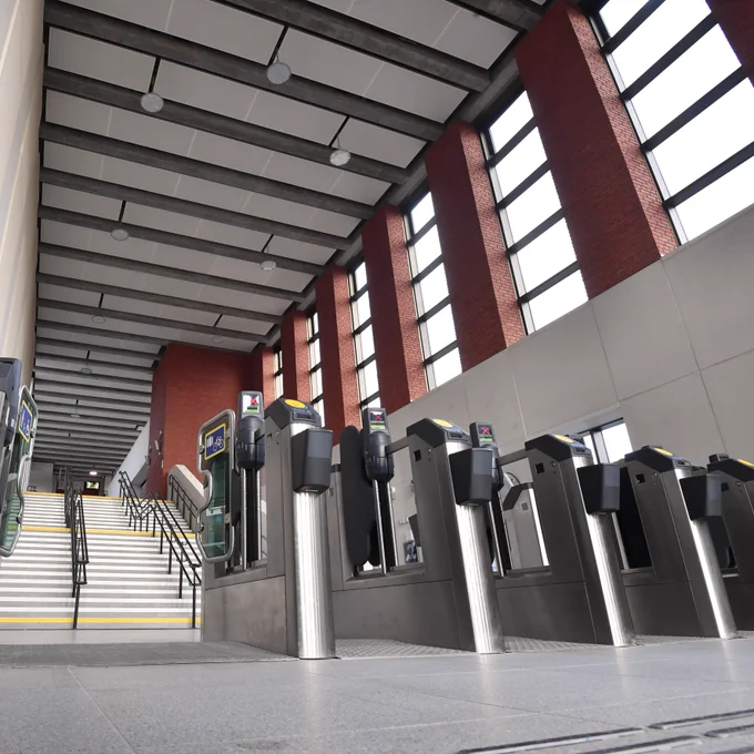 An image of the new University station building looking up a long staircase with double height ceiling above, large windows which flood the concourse with extra light and a multi channel ticket gateline. 