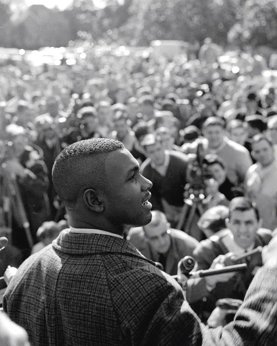 A photo of Harvey Gantt in the foreground looking to his right with a crowd in front of him.