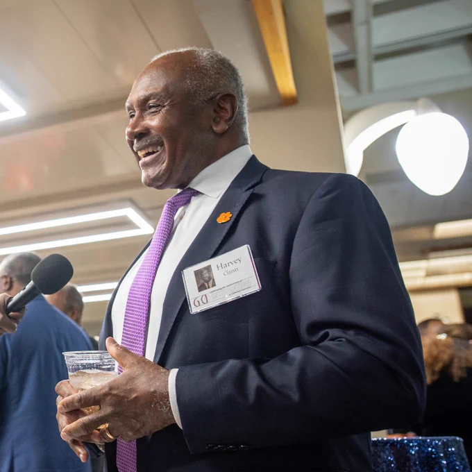 Harvey Gantt wearing a suit and tie smiling while speaking into a microphone.
