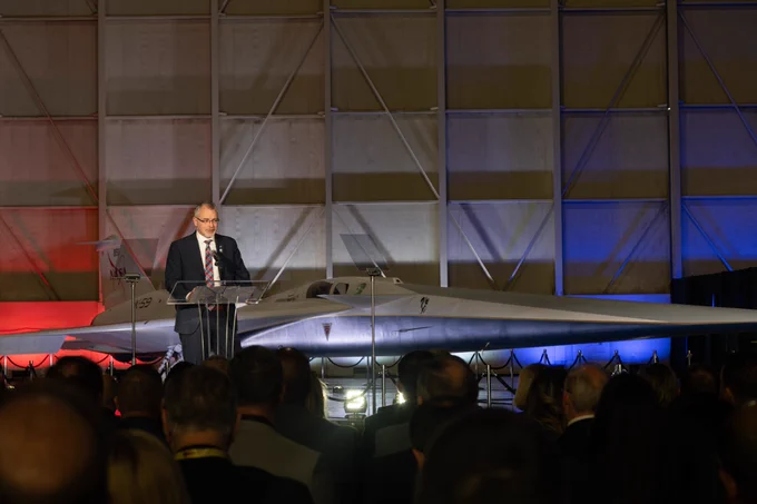 NASA Associate Administrator Jim Free speaks at a podium on stage in front of NASA's X-59 experimental supersonic aircraft at its unveiling at Lockheed Martin Skunk Works in Palmdale, California, on Friday, January 12, 2024.