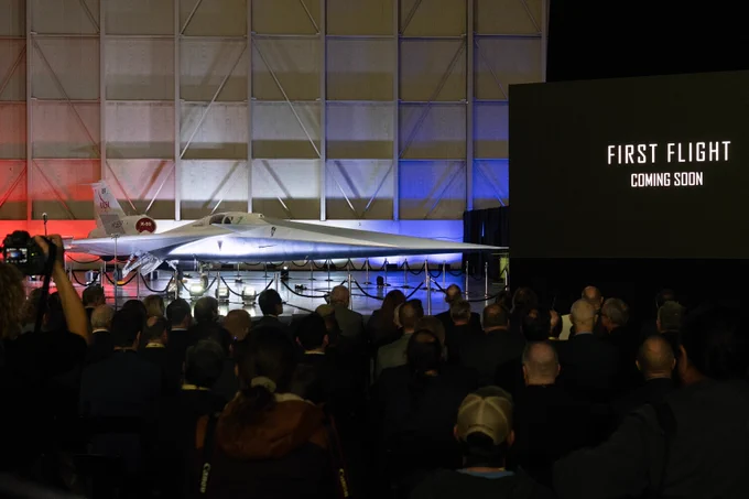 NASA's X-59 experimental supersonic aircraft is displayed at its unveiling at Lockheed Martin Skunk Works in Palmdale, California, on Friday, January 12, 2024. An audience is in the foreground, and a screen says, "First Flight | Coming Soon."