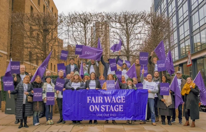 Photo shows large group of Equity members holding a large purple banner which reads 'Fair Wage On Stage' and waving purple Equity flags