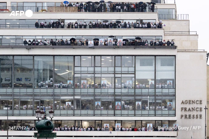 Agence France-Presse (AFP) employees stand on the balconies and at the windows of the agency's headquarters in Paris, on January 17, 2024, holding portraits in support of AFP journalists working in Gaza.
