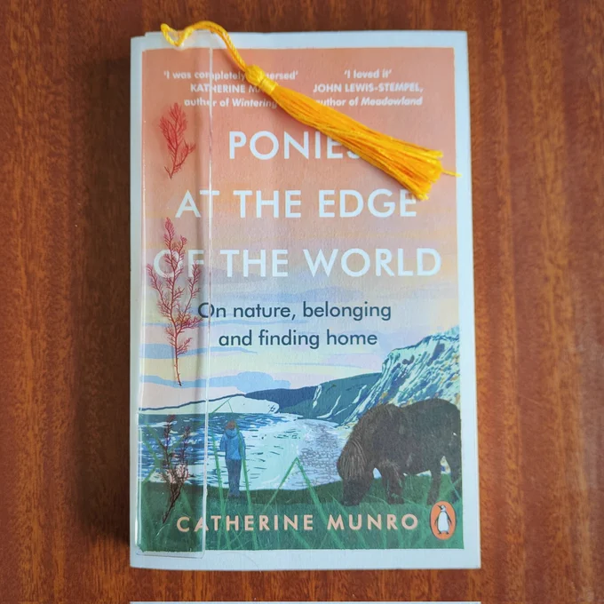 Image shows a copy of Ponies at the Edge of the World with clear bookmarks with red seaweed andgold tassel 