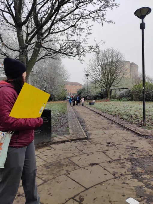 A tour guide with a yellow binder stands in front of a path that leads to Clifford's Tower.