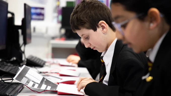 Two students are seated at a desk, working on their coding projects. 