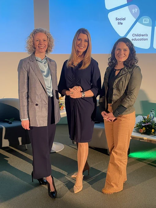 Three women, Claire McGee, Gina London and Prof Deirdre O’Shea, standing in front of a large screen smiling at the camera.