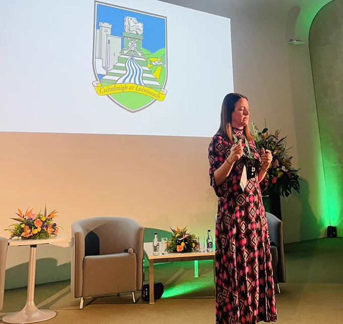 Caroline Currid speaking in front of a large screen with the logo of the Limerick hurlers displayed behind her