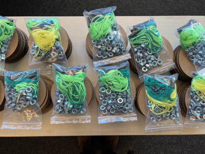 Stacks of cardboard disks each with a plastic bag on top filled with springs, cords, and (screw) nuts