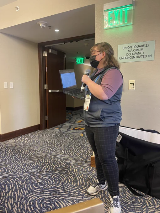 The Collective Program Coordinator speaking into a microphone engaging with participants. 