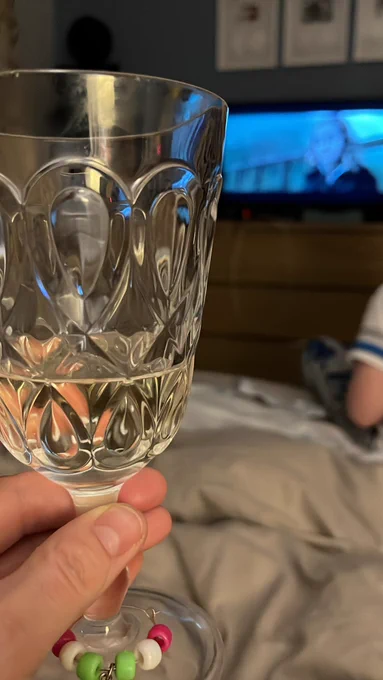 Wine glass filled with white wine is held up. Behind is a tv showing a film (Harry Potter!)