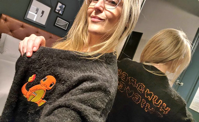 Rachel selfie in a black Pokemon x 100 Thieves cardigan with "HUNDRED THIEVES" in orange stitch bubble letters across the back, reflected in mirror