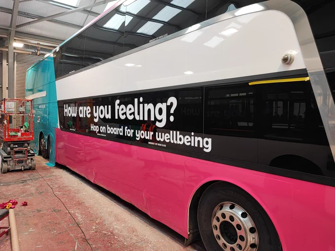 A Stagecoach bus is painted in SAMH colours (pink and teal) with text "How are you feeling? Hop on board for your wellbeing"