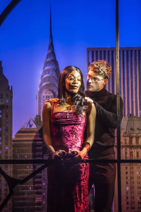 Rhianne-Louise McCaulsky and Daniel Bravo onstage - Daniel massaging Rhianne’s shoulders, as they stand in front of a city skyline.