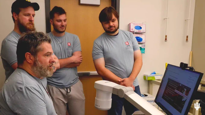 Four people in grey IUPUI t-shirts gather around a computer.