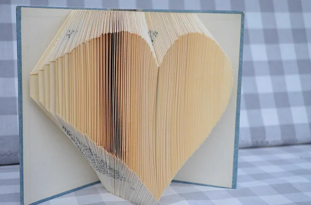 A hardcover book with its pages folded to create a 3D heart shape. 