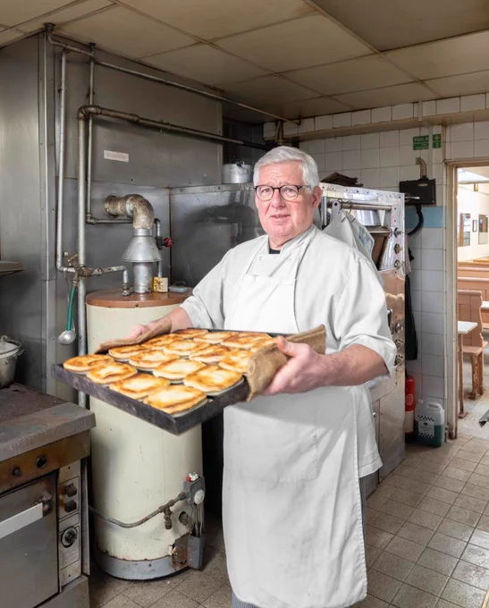 A photograph of a baker holding a tray of pies.