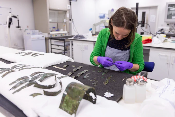 Conservator Bethan Bryan in the conservation lab with a large number of brass fragments prior to the reconstruction of the arm guard. 