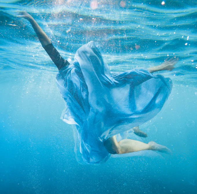 Artwork for the show featuring a person underwater wrapped in fabric. The sun is shining through the water and their arms and legs are gracefully outstretched.