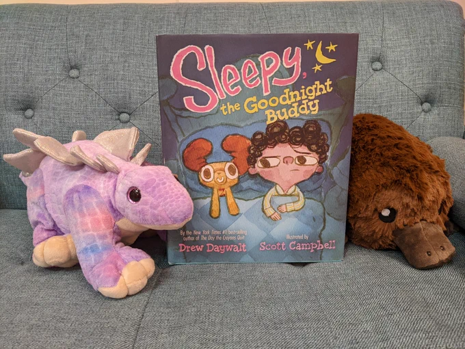 Lilac the dinosaur and Astrid the Platypus posing next to a book