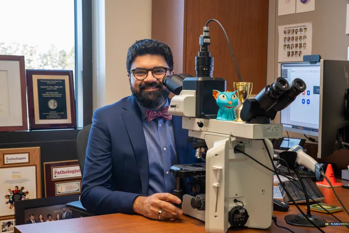 Dr. Kamran Mirza sits at his microscope while smiling at the camera. 