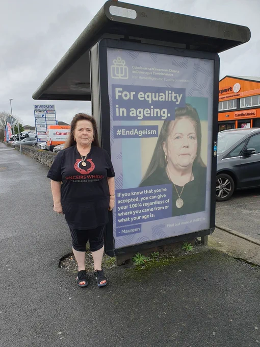 Maureen Ward standing beside bus shelter advertisement of Maureen in the IHREC #EndAgeism campaign.