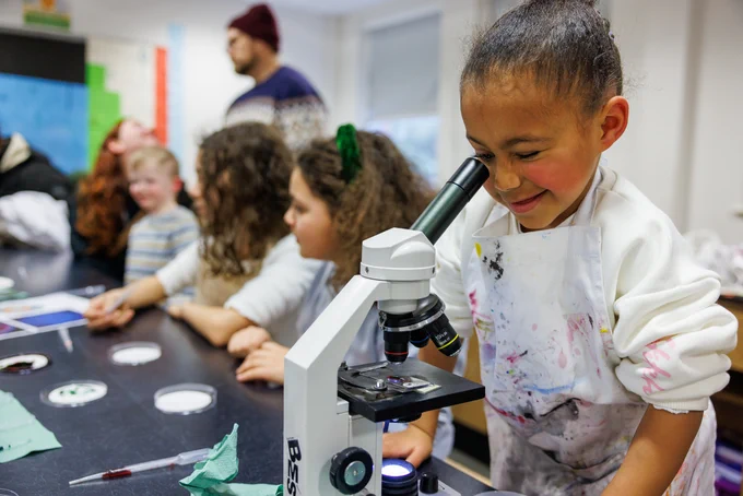 Little girl peering through a microscope and smiling. 