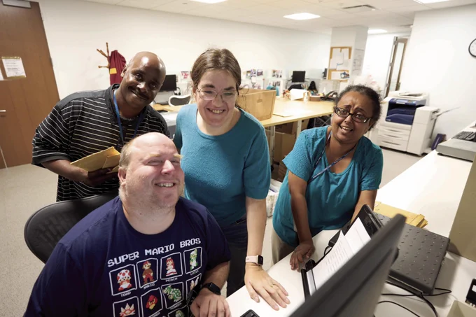 A photo of four people smiling for the camera in an office environment.