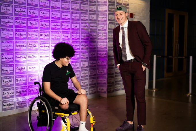 Roope stands in his suit and laughs as Jayden admires his shoes