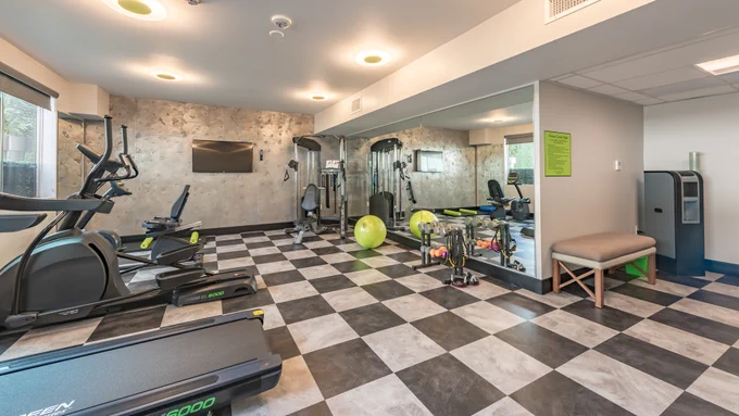 Lexen Hotel North Hollywood fitness gym with workout machines: treadmill, elliptical, bike, weight machine, exercise ball, TV, water station.