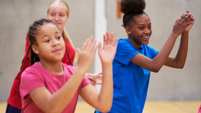 Group of girls smiling and clapping their hands as they take part in an activity.