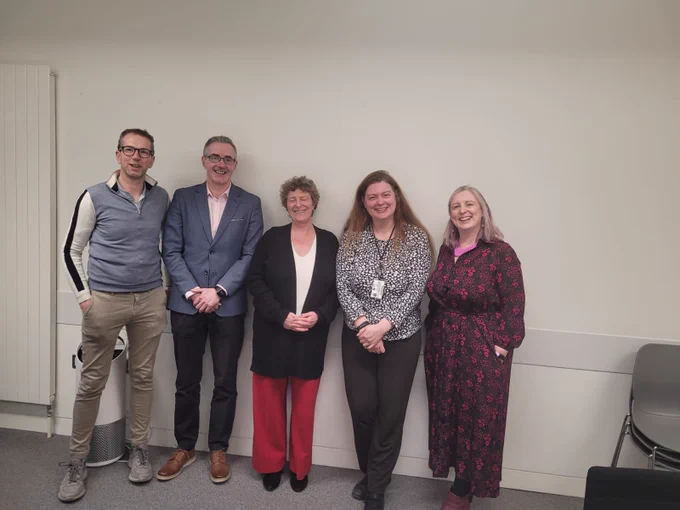 Two men and three women standing against a white wall. In the center is Dr Pauline Morley.