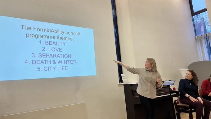 Workshop leader Ruth Montgomery points at a screen that leaves Themes: Beauty, Love, Separation, Death and Winter, City Life