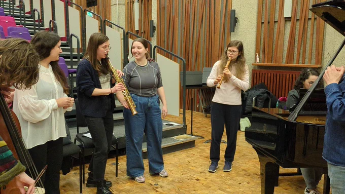 A music workshop with Deaf actor Rhiannon May. A grand piano is in the corner, while 4 people stand together. One person playing the recorder and another the clarinet
