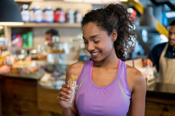 A young woman eats a protein bar at a café after exercising
